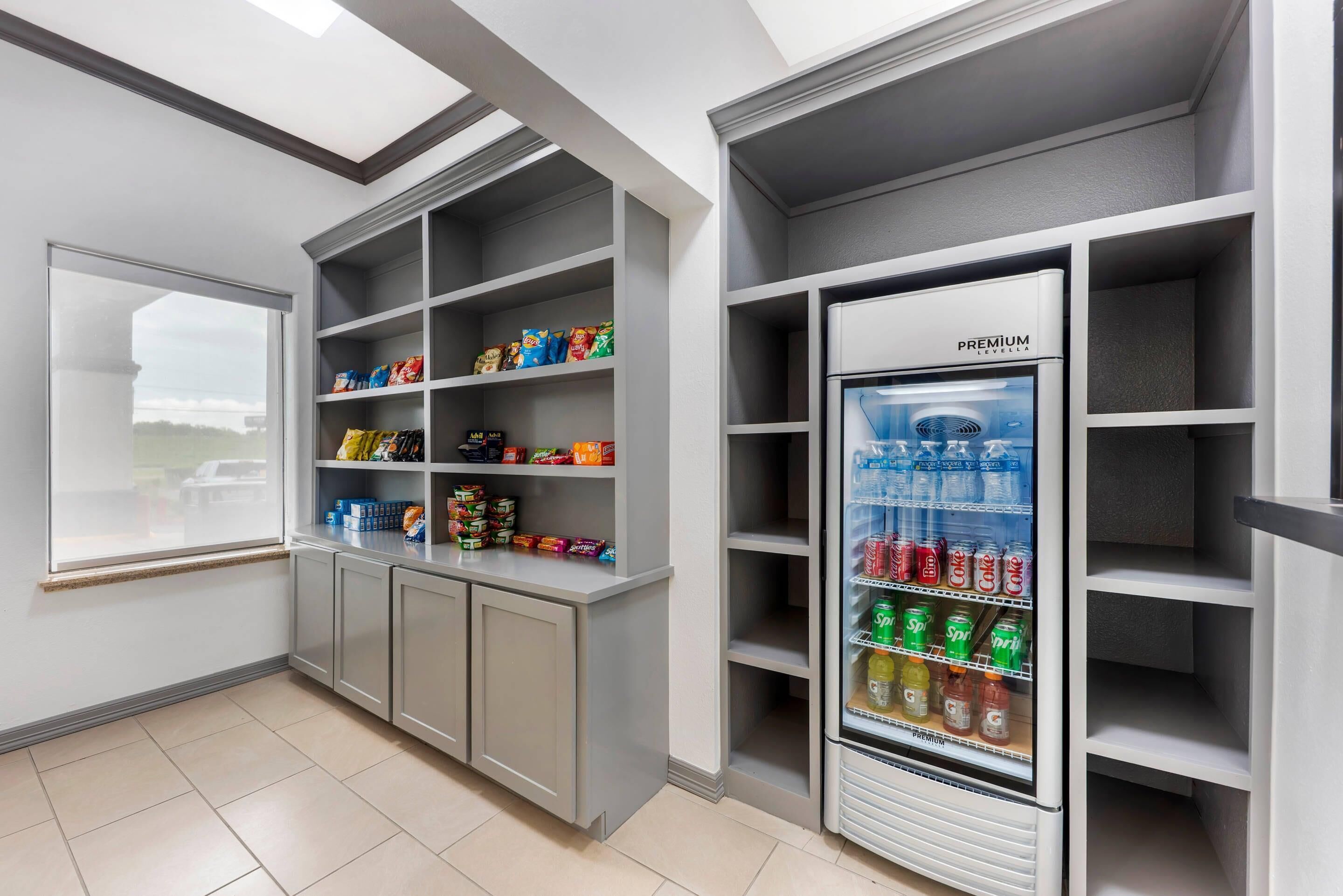 A modern kitchenette with grey cabinetry, a built-in refrigerator, and a window providing a view of the outside.