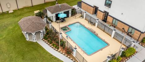 A swimming pool with a hot tub, a covered patio, and a small gazebo.