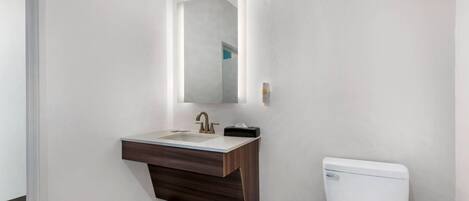 A bathroom with a white toilet, a dark wood vanity with a sink, and a mirror above the vanity.