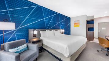 Una habitación de hotel moderna con una cama grande, un sillón gris, un escritorio y una pared con estampado azul.