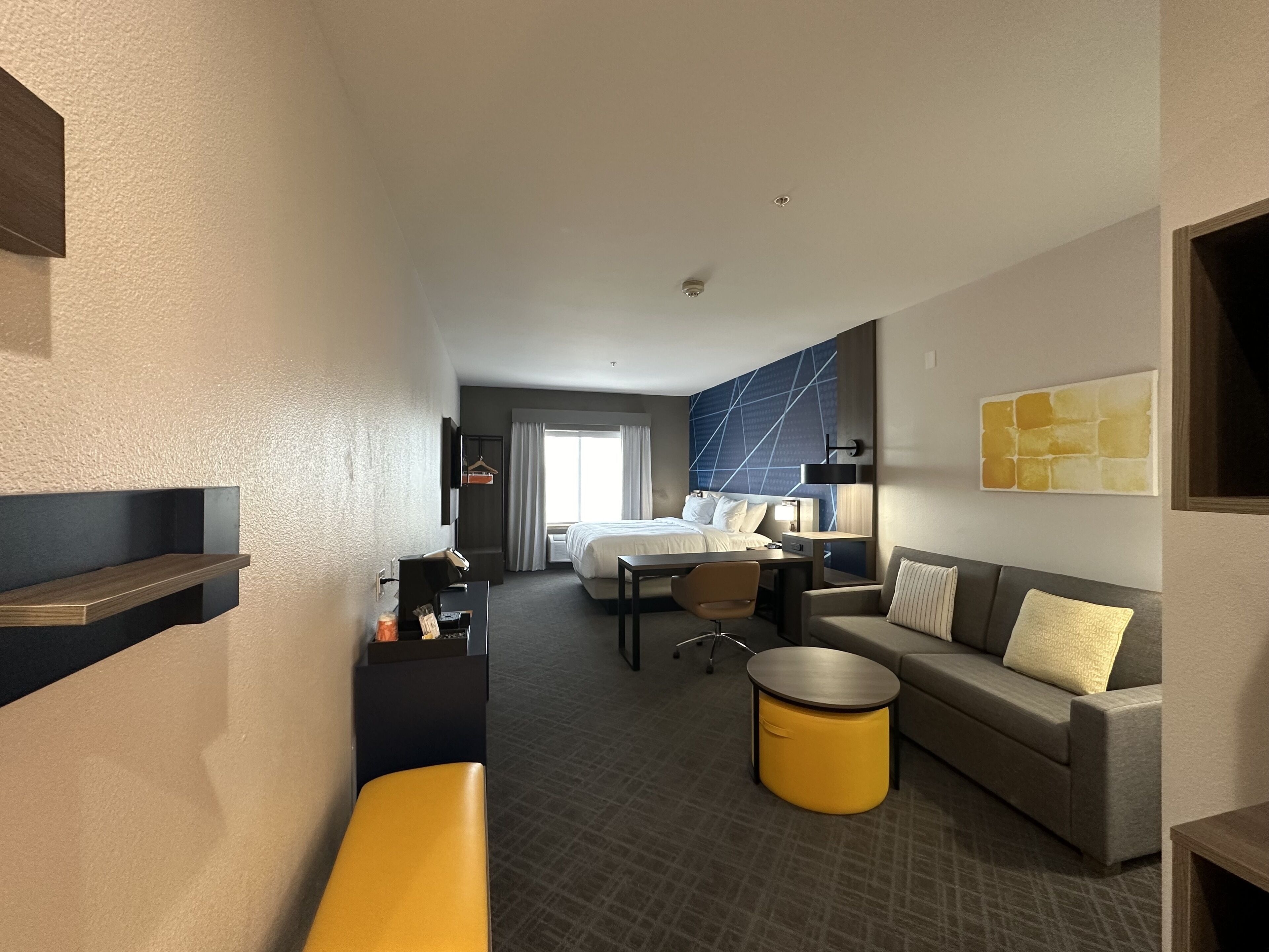 Ett hotellrum med en säng, ett skrivbord, en soffa, en bänk och ett litet bord.