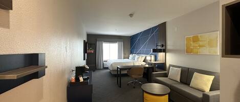 A hotel room with a bed, a desk, a sofa, a bench, and a small table.