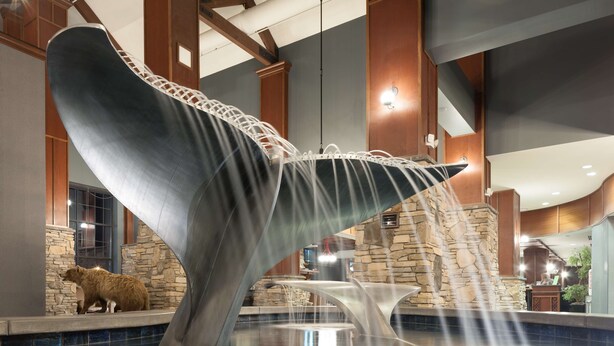 A large whale tail sculpture in a lobby with a stone wall and a reception desk. - Embassy Suites by Hilton Anchorage (Anchorage)