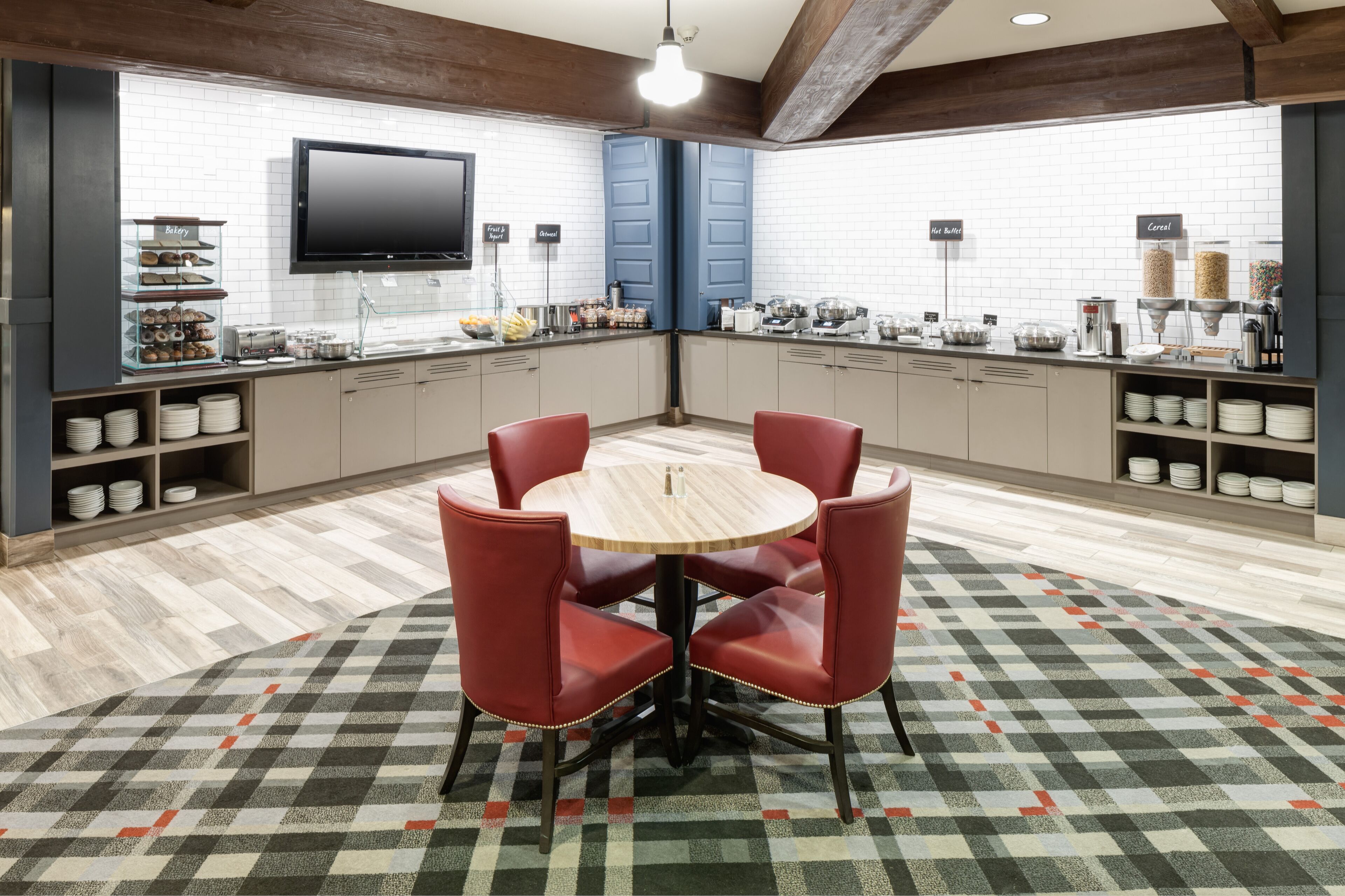 A modern kitchen with a round table and red chairs, white tiled backsplash, and various food dispensers.