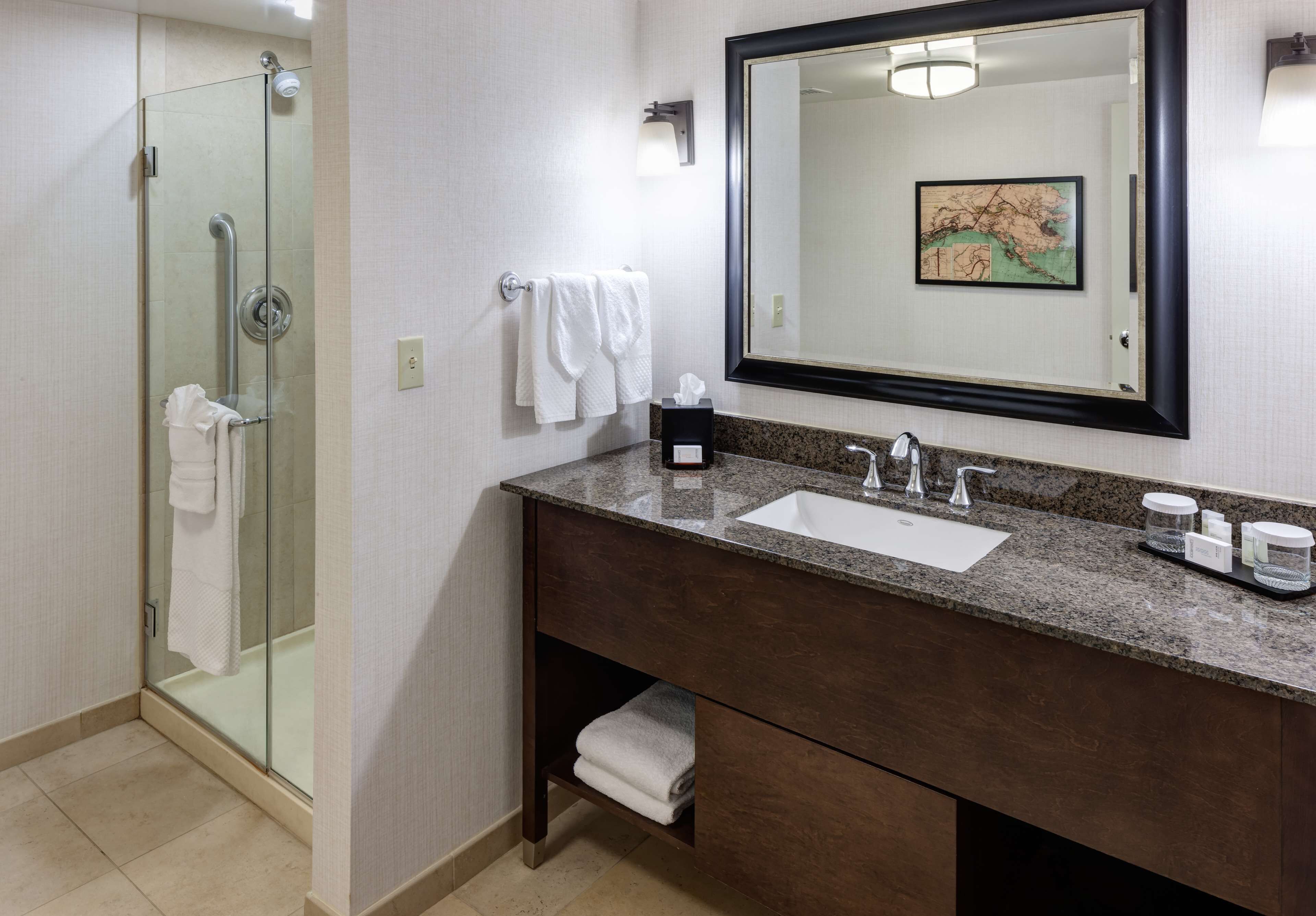A bathroom with a glass shower enclosure, a sink with a dark countertop, and a large mirror with a map.