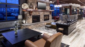 A modern living room with a stone fireplace, leather seating, and a large TV mounted on the wall. - Embassy Suites by Hilton Anchorage (Anchorage)