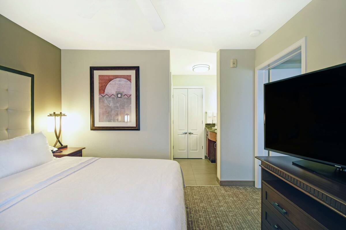 Habitación de hotel con cama, televisión, un cuadro en la pared y una puerta que da al baño.