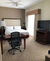 A hotel room with a bed, desk, chair, television, and a ceiling fan.