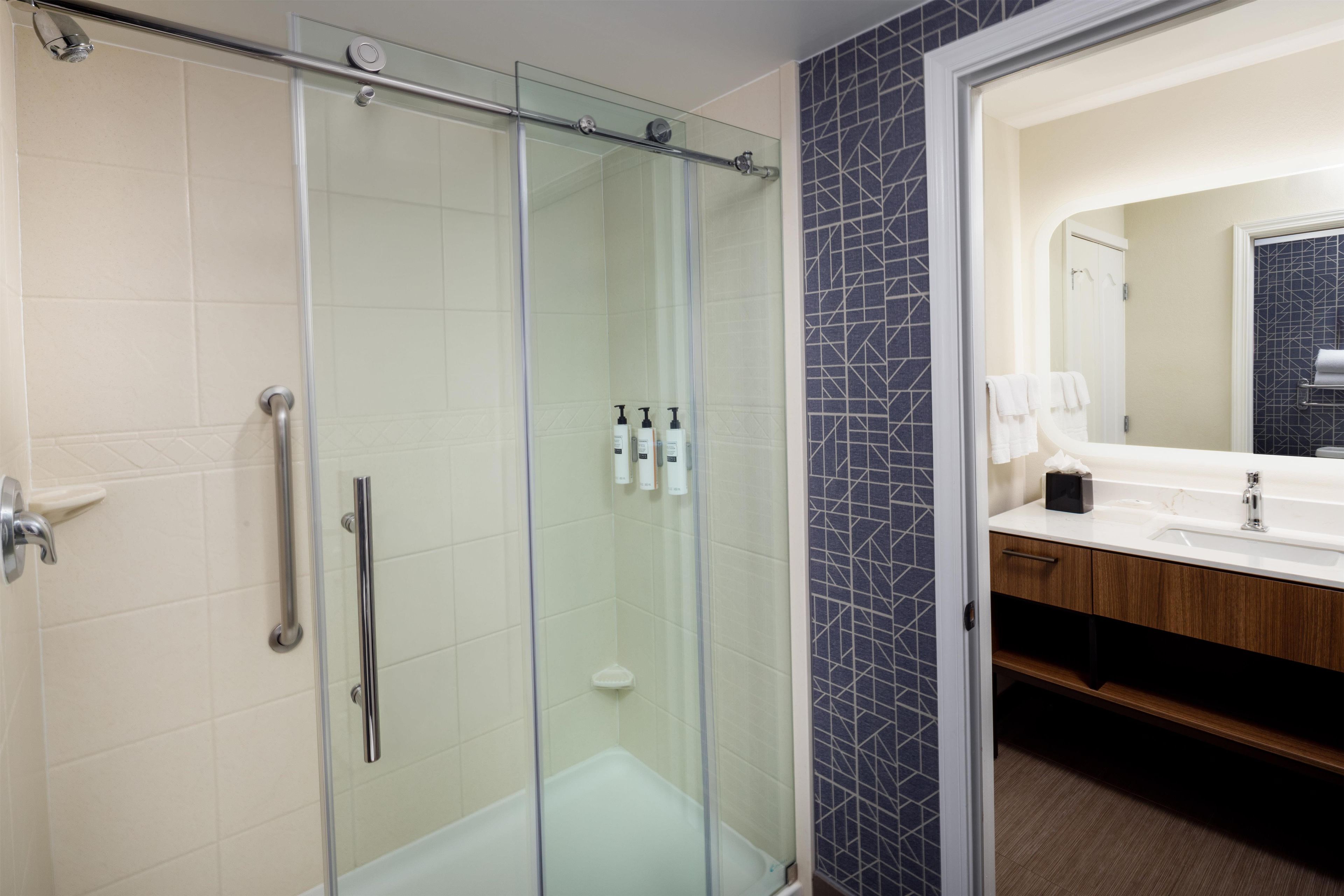 Un baño moderno con cabina de ducha de vidrio, tocador con espejo y lavamanos.