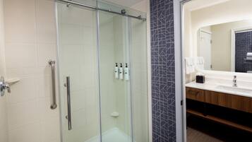 Un baño moderno con cabina de ducha de vidrio, tocador con espejo y lavamanos.