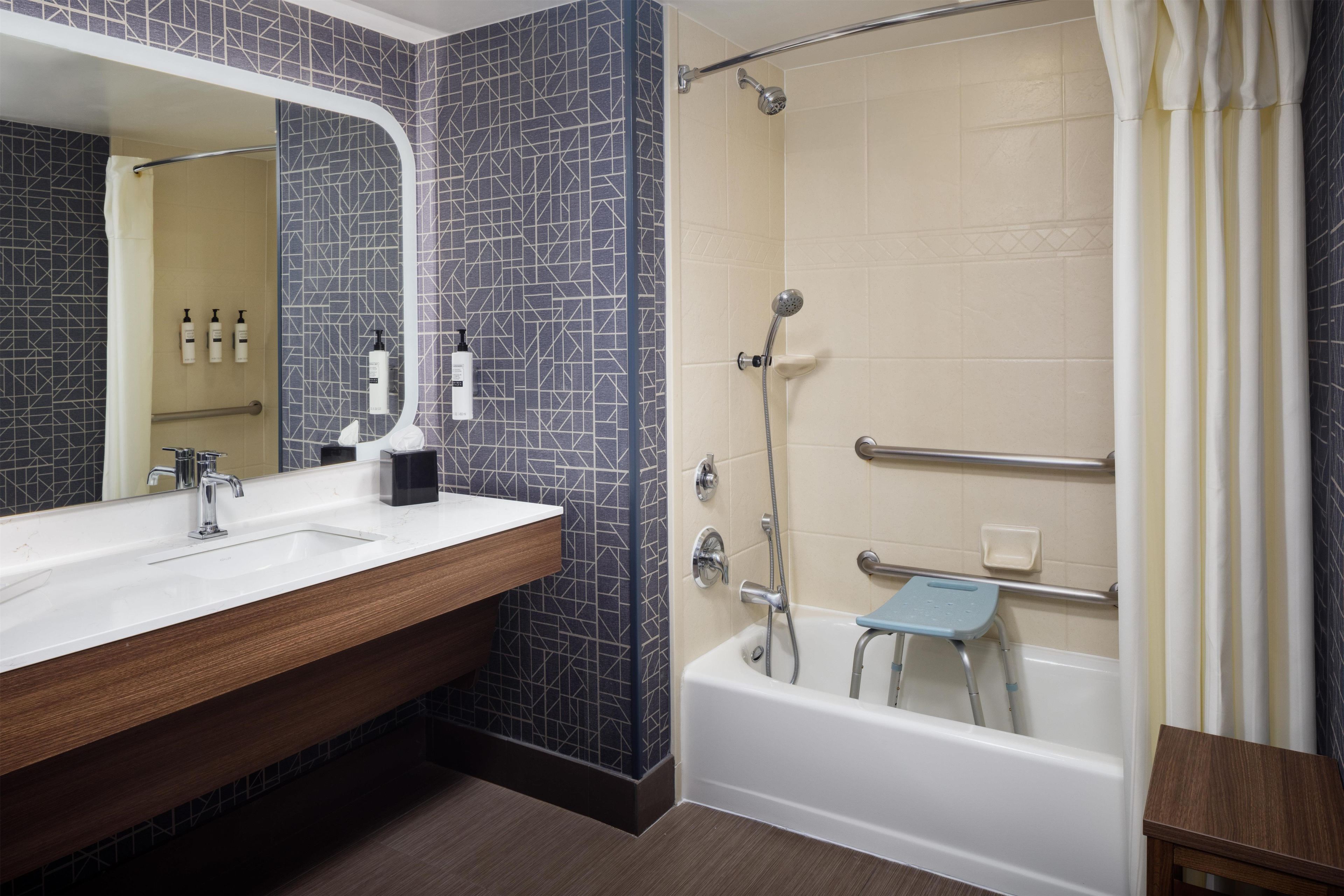 A bathroom with a white sink, a mirror, a shower with a handheld showerhead, and a small step stool.