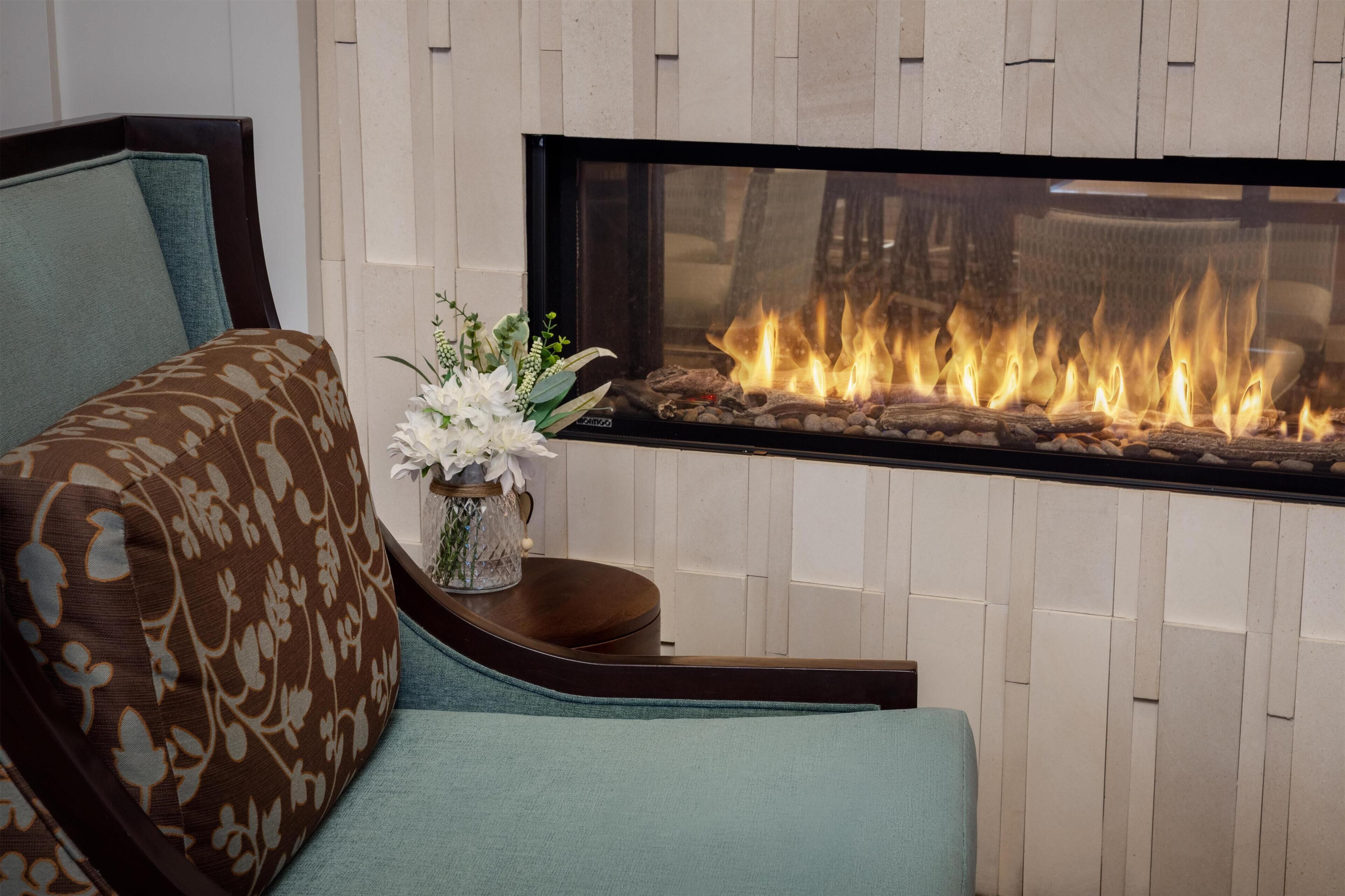 A modern living room with a sofa, a side table with a vase of flowers, and a fireplace with visible flames.