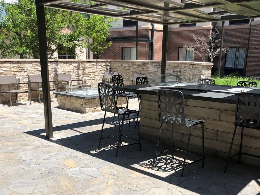 Un área de patio al aire libre con piso de piedra, sillas de metal y una mesa con cubierta de vidrio.