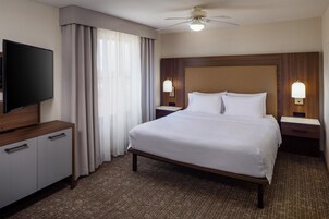 A hotel room with a bed, a television, a desk, and a ceiling fan.
