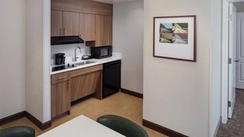 A compact hotel kitchen with a microwave, coffee maker, and a sink. There is a framed picture on the wall and a door leading to another room.