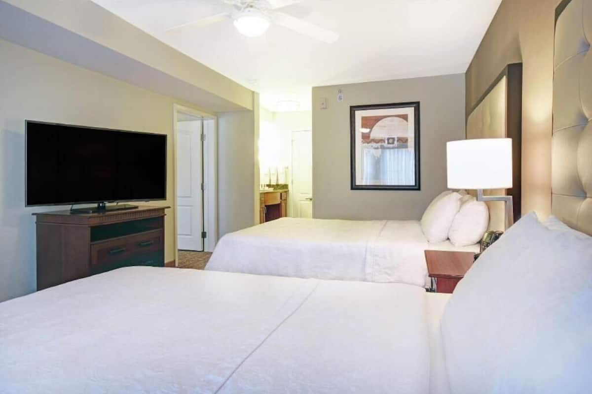 Habitación de hotel con dos camas, televisión, un cuadro en la pared y ventilador de techo.