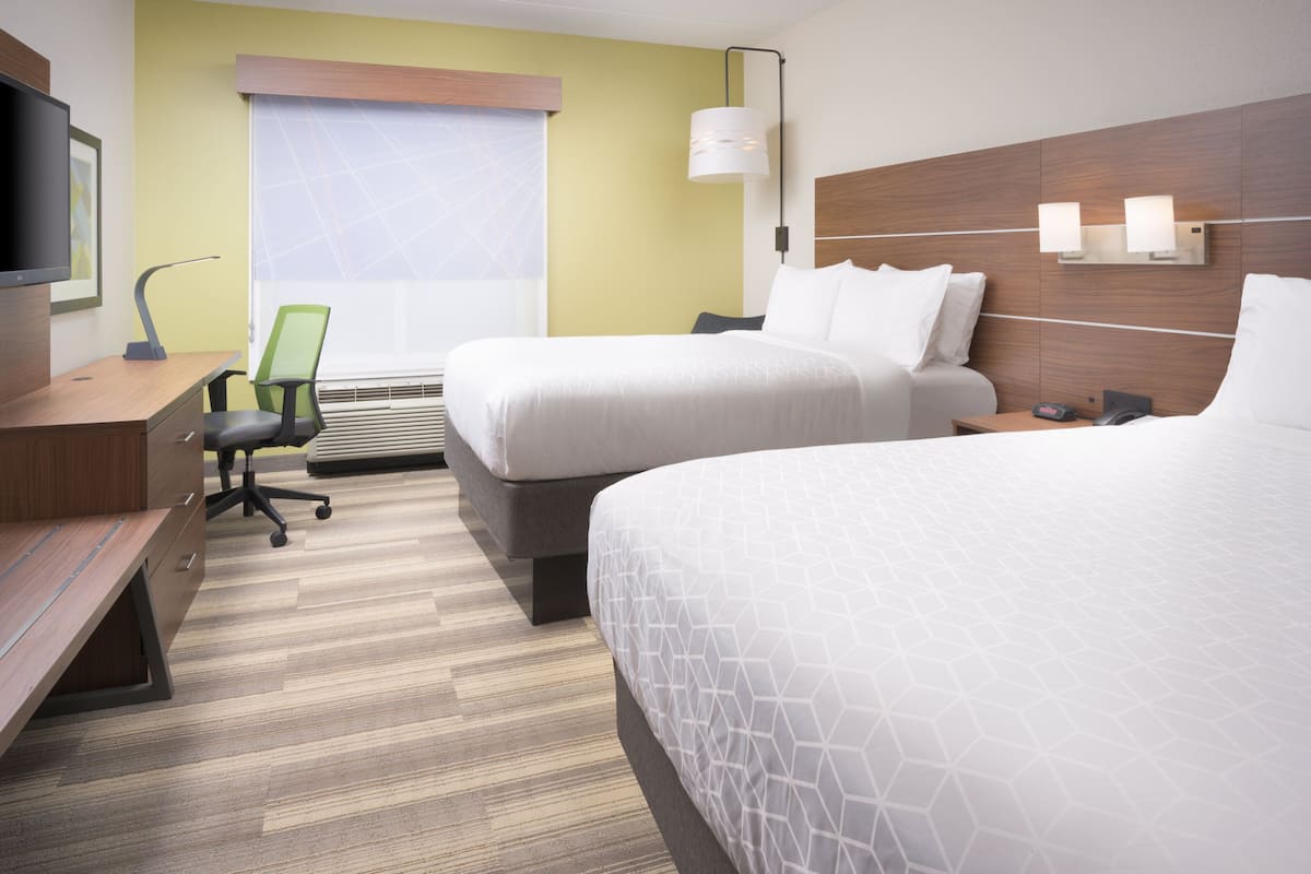 Une chambre d’hôtel avec deux lits, un bureau avec une chaise, une télévision et une fenêtre avec des stores.