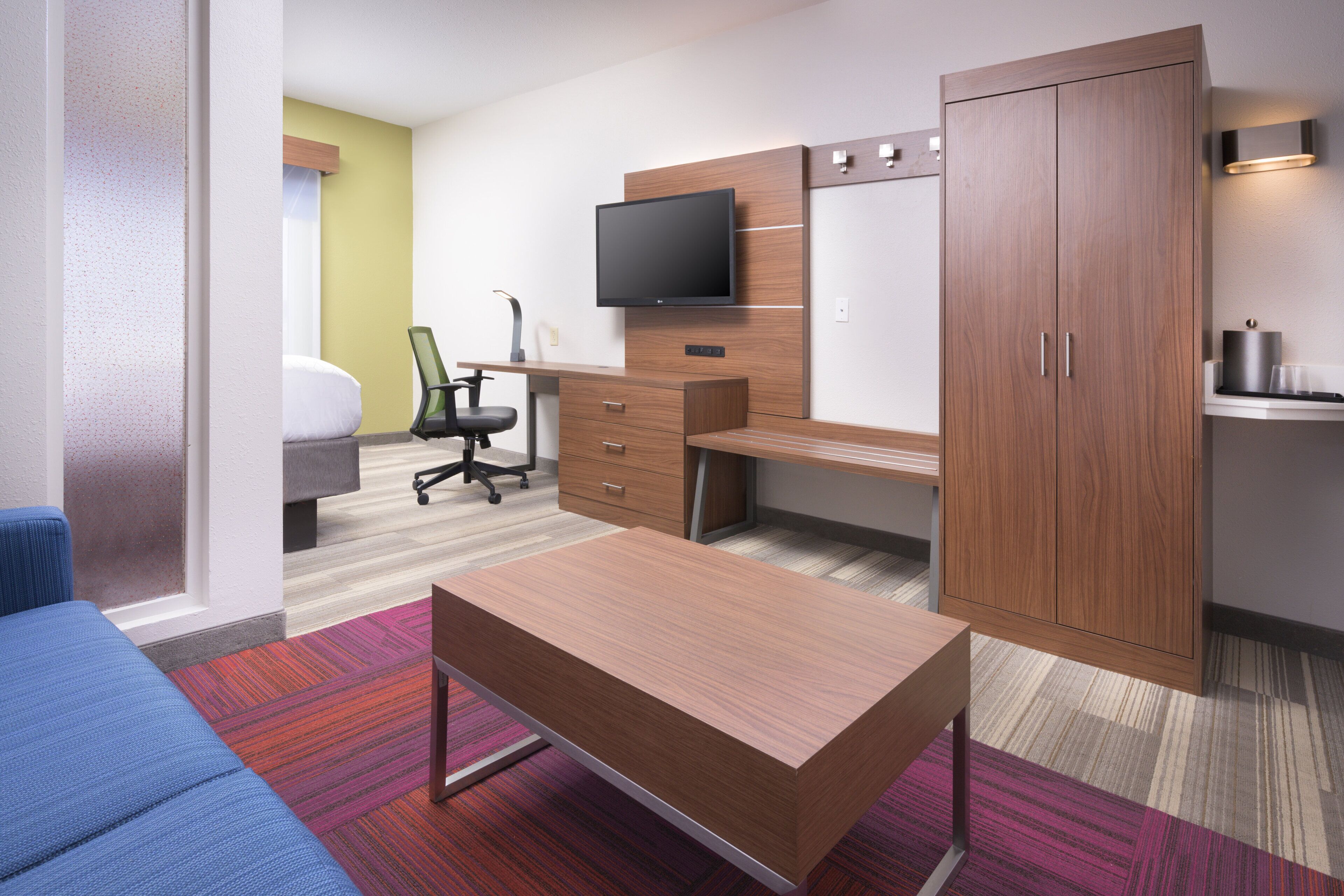 A hotel room with a bed, a desk, a TV, a wardrobe, and a blue sofa.