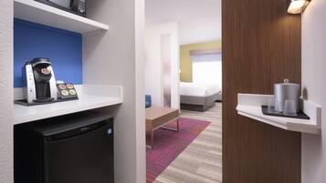 Quarto de hotel compacto com cozinha compacta, uma cama, mesa de cabeceira e janela com cortinas.