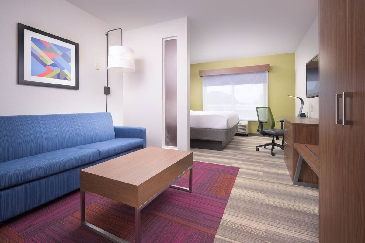 Une chambre d’hôtel avec un canapé bleu, une table en bois, un lit avec une chaise verte, un bureau et un téléviseur.