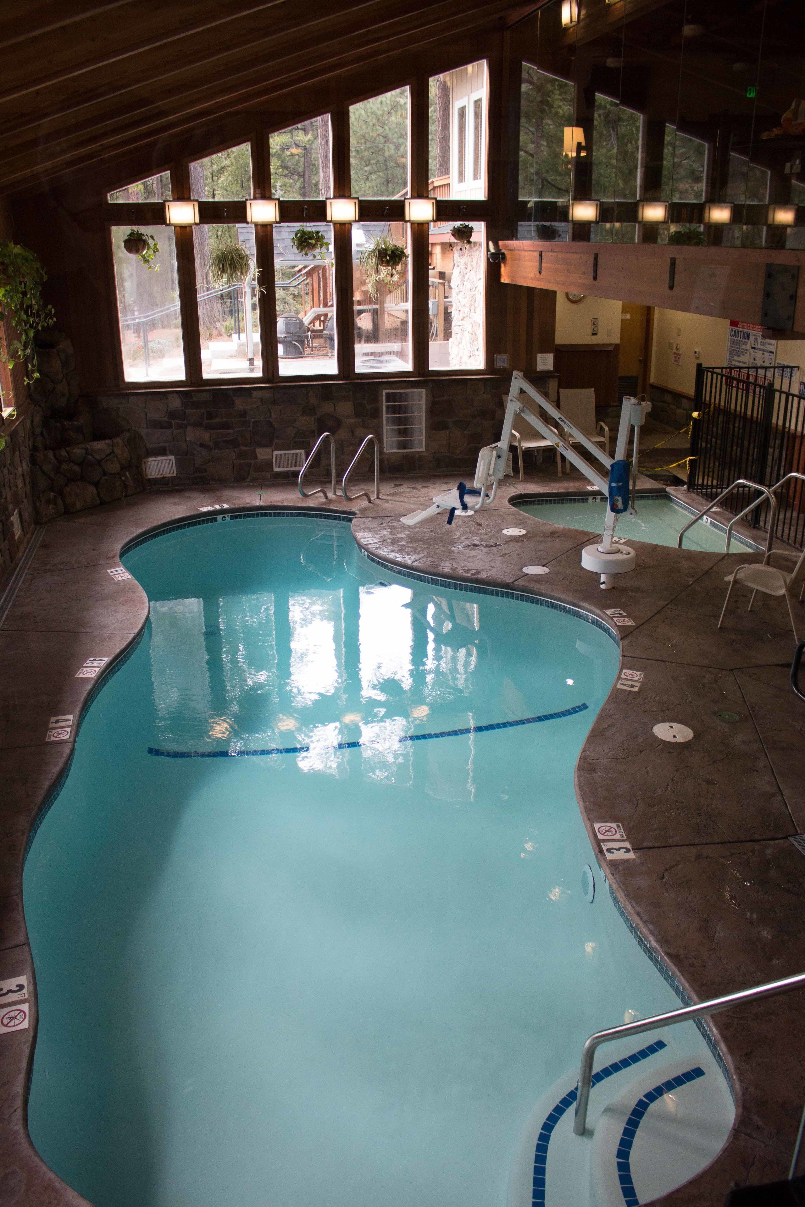 Une piscine intérieure à l’eau claire, entourée de murs en pierre et dotée de grandes fenêtres.