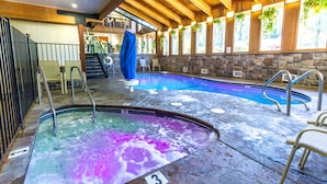 A hot tub area with a stone wall, wooden ceiling beams, and a view of the outdoors through large windows. - Mountain Retreat Resort (Arnold)
