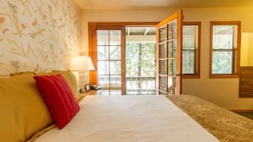A hotel room with a bed, a nightstand, a lamp, and a view through a door to an outdoor area.