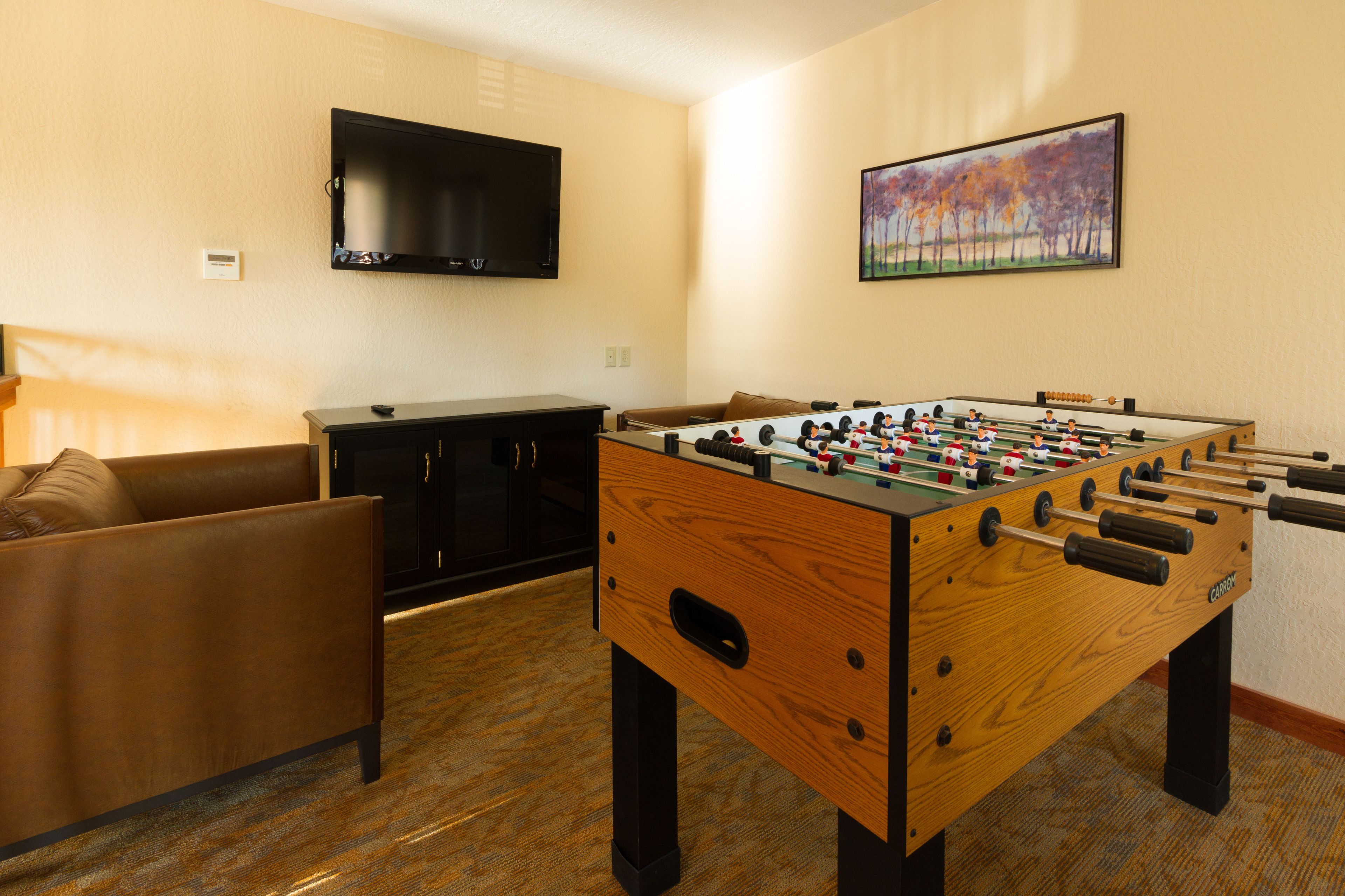 A room with a foosball table, a TV mounted on the wall, a sofa, and a painting.