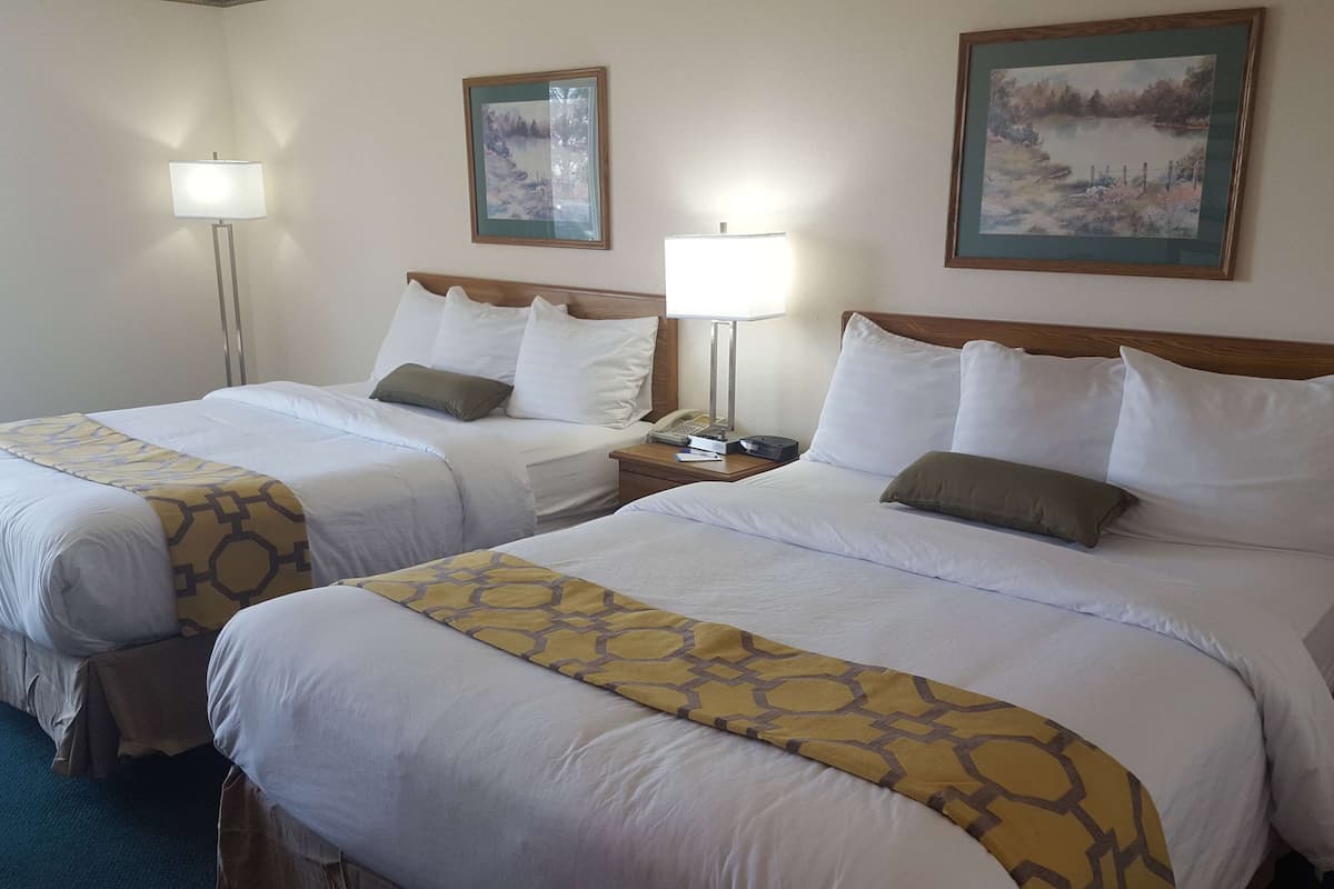 A hotel room with two beds, each with white bedding and a patterned throw. There are two bedside lamps, a telephone, and a small table with a lamp.