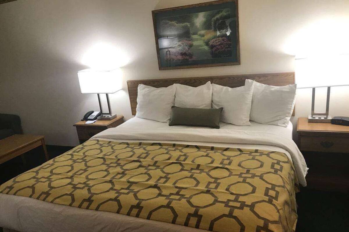 A hotel room with a large bed, two bedside tables, a nightstand, a lamp, a painting on the wall, and a wooden headboard.