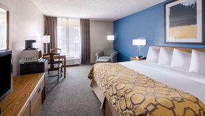 A hotel room with a bed, a desk with a coffee maker, a chair, a lamp, and a painting on the wall. - Baymont by Wyndham Limon (Limon)