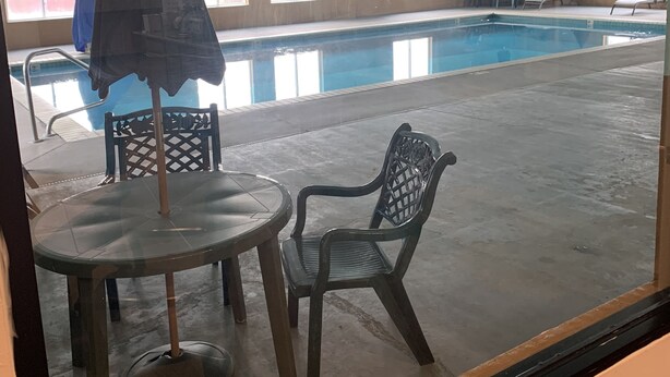 An indoor swimming pool with a view through a window. There are lounge chairs and a table with an umbrella. - Baymont by Wyndham Limon (Limon)