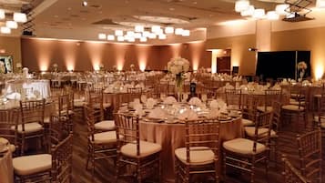 A banquet hall with round tables, wooden chairs, and chandeliers.