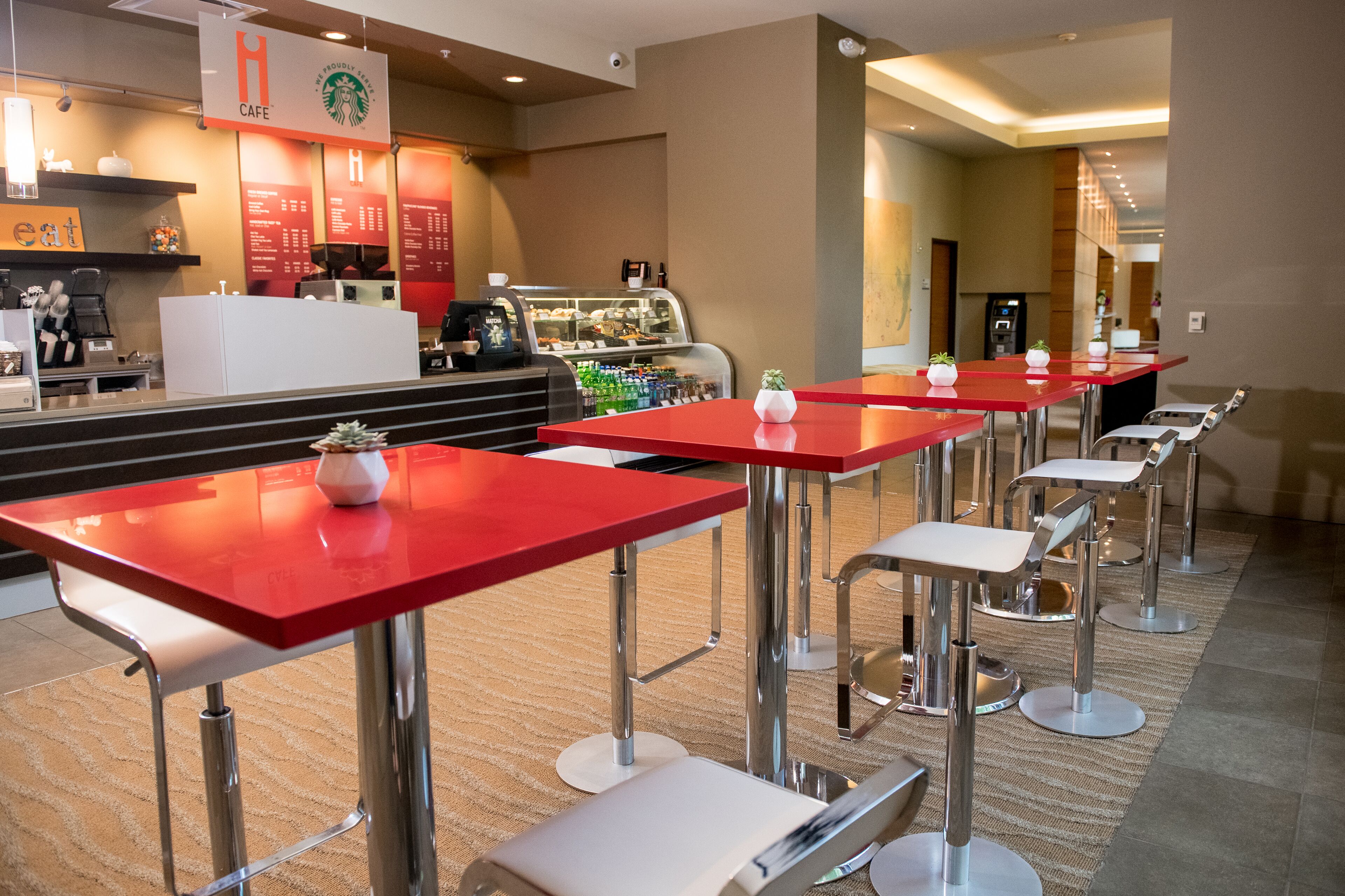 A modern cafe with red tables and white chairs, a Starbucks sign, and a counter with a coffee machine.