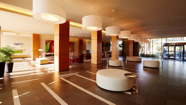 Eine großzügige Lobby mit moderner Möblierung, großen weißen Pendelleuchten und einer zentralen Lounge.
