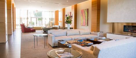A modern hotel lobby with a large sofa, a coffee table, and a TV screen.