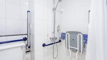 A bathroom with white tiles, a shower with a handheld showerhead, a toilet with a grab bar, and a soap dispenser.