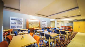 Uma área de refeições de hotel com várias mesas e cadeiras, piso estampado e quadros nas paredes.