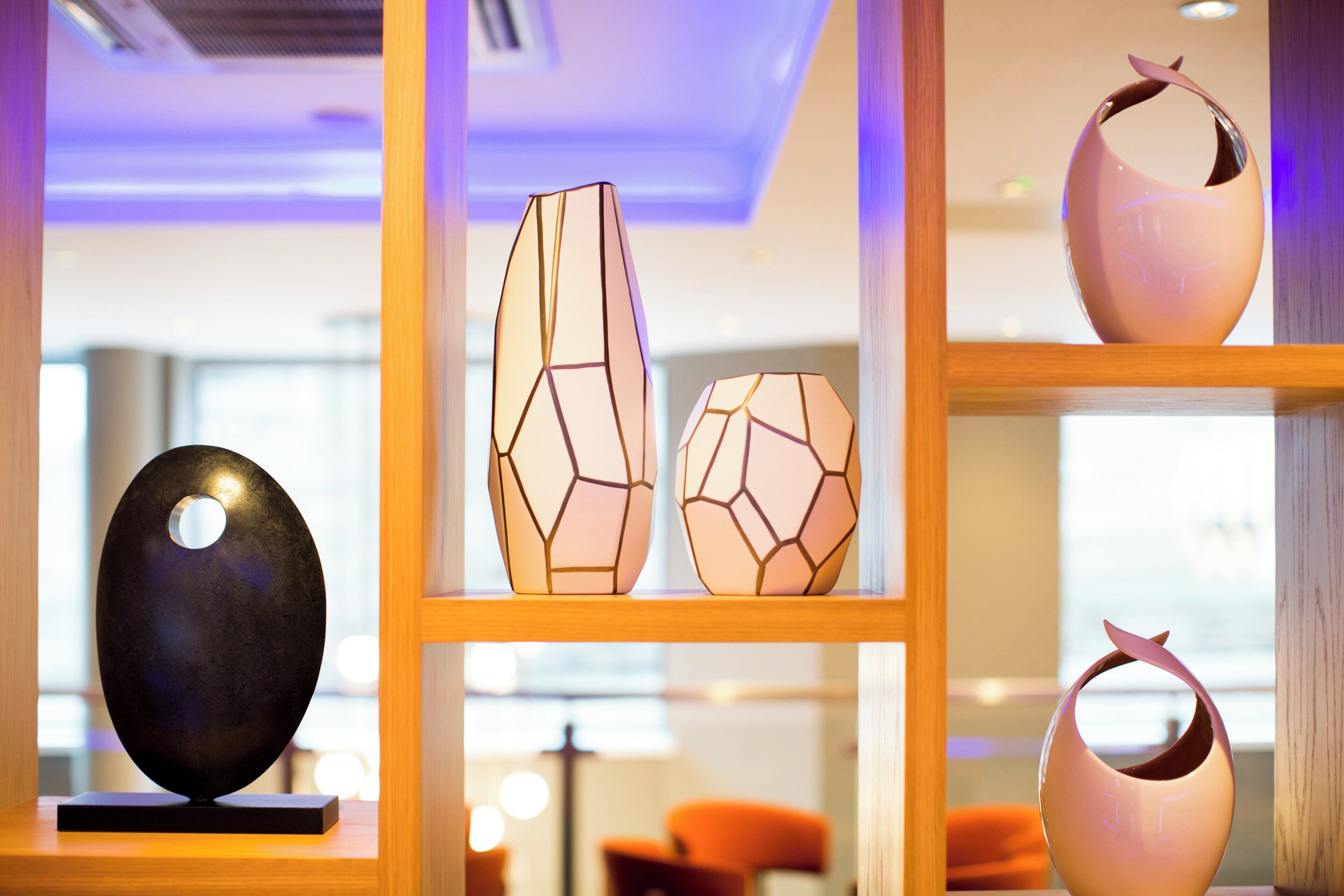 A modern interior with a black spherical sculpture on a wooden pedestal, geometric vases on shelves, and a wooden-framed window.