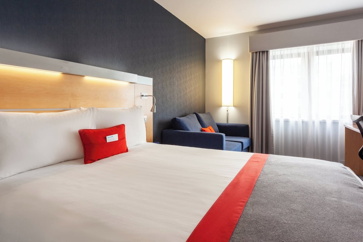 A hotel room with a large bed, a desk, a chair, and a window with curtains.