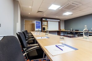 A conference room with a long table, chairs, a whiteboard, and a projector screen.