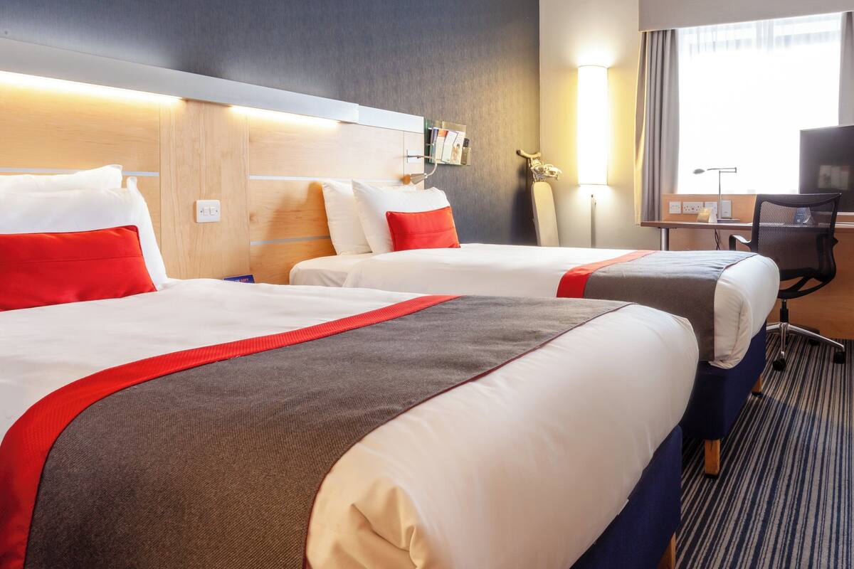 A hotel room with two beds, each with red and white bedding, a desk with a chair, and a TV.