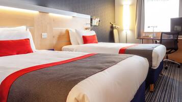 A hotel room with two beds, each with red and white bedding, a desk with a chair, and a TV.