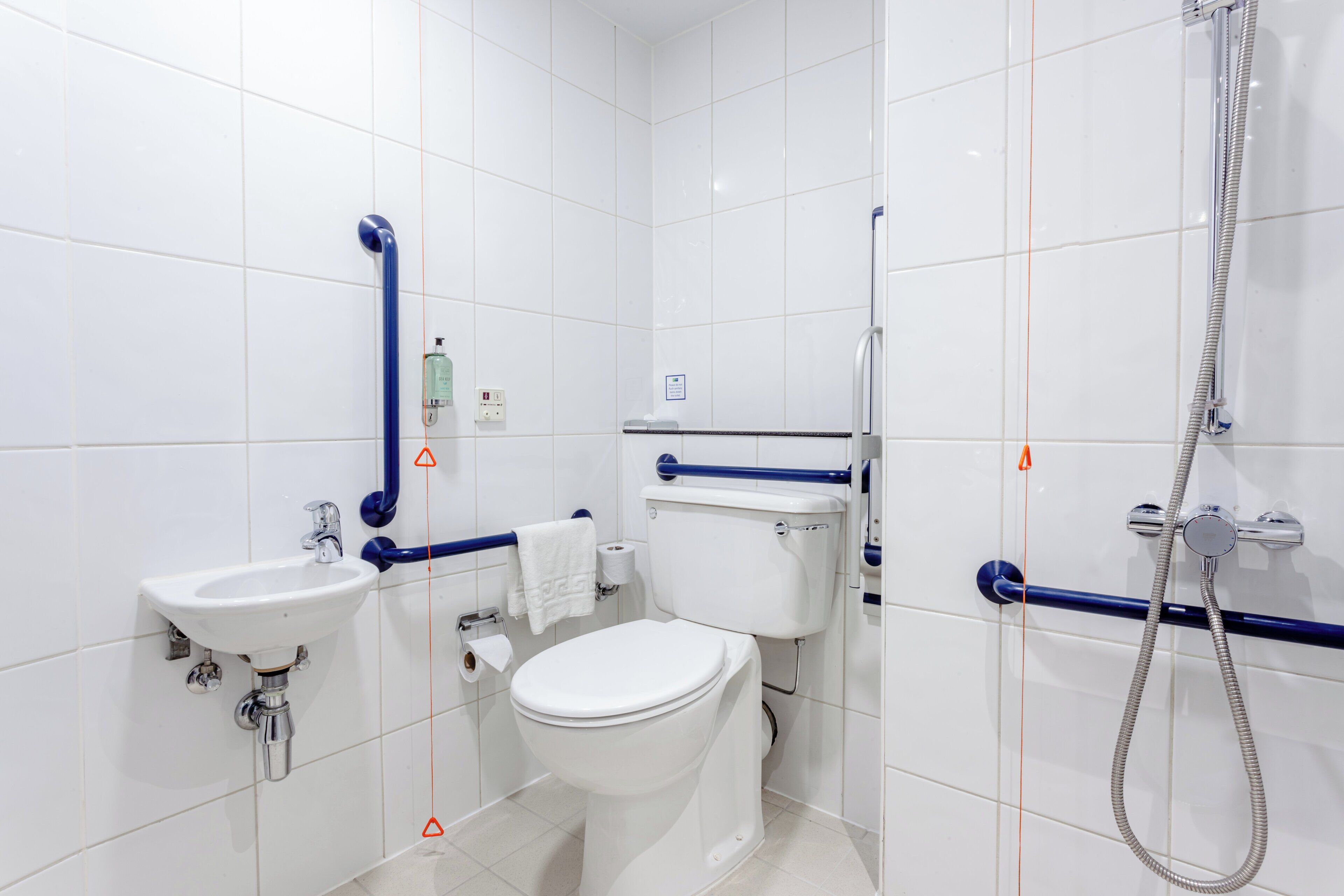 A modern bathroom with white tiles, a white sink, a toilet, and a shower with a handheld showerhead.