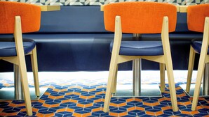 A row of chairs with wooden legs and orange fabric backs, positioned in front of a dark-colored sofa against a patterned wall. - Holiday Inn Express Edinburgh Royal Mile by IHG (Edinburgh)
