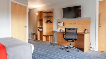 A hotel room with a bed, a desk with a chair, a TV, and a wardrobe.