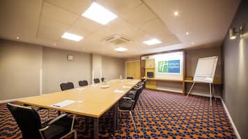A conference room with a long table, chairs, a whiteboard, and a projector screen.