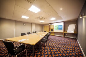 Une salle de conférence équipée d’une longue table, de chaises, d’un tableau blanc et d’un écran de projection.