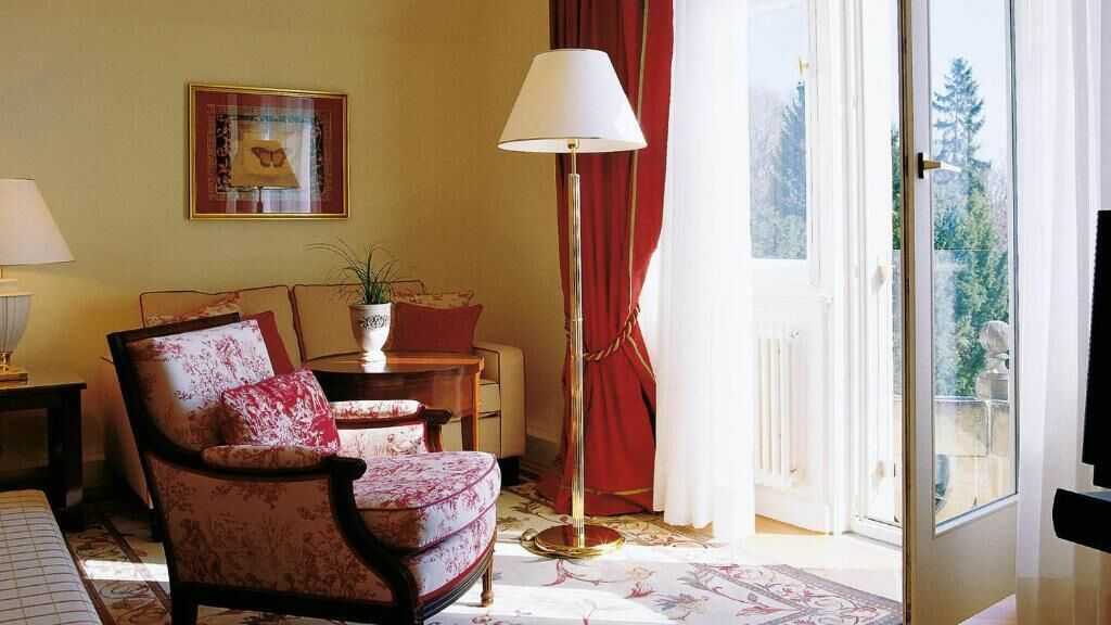 Een woonkamer met een stoel, een lamp, een plant en een schilderij aan de muur.