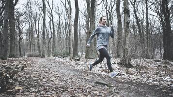 A person running in a forested area with leaf-covered ground.